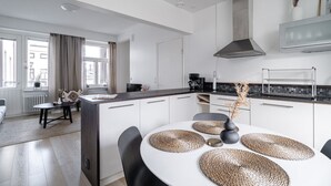 Una cocina moderna con armarios blancos, encimera oscura y comedor con mesa redonda y individuales tejidos.