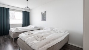 Ein Hotelzimmer mit zwei Betten, einem Fenster mit Vorhängen, einer Pendelleuchte und einem gerahmten Bild an der Wand.