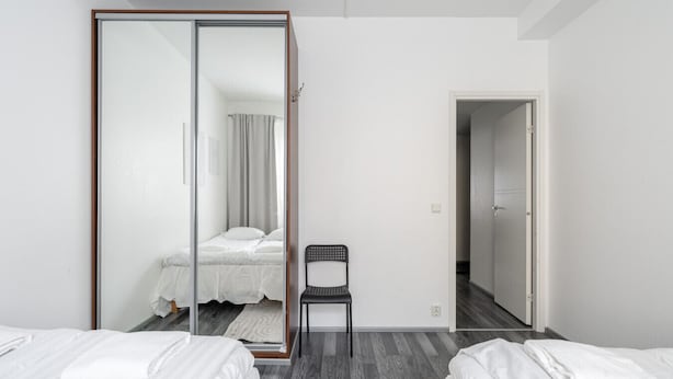 A hotel room with two beds, a chair, a wardrobe, and a bathroom visible through a sliding door.