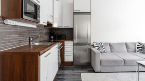 A modern kitchen with a built-in oven, microwave, and refrigerator, a grey sofa with patterned cushions, and a wooden countertop.