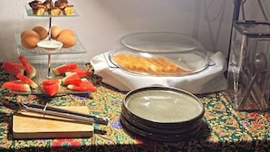 A table with a colorful tablecloth, a stand with eggs, a stand with pastries, a bowl of soup, and a stand with sliced watermelon. - Heritage House 123 (George Town)