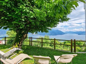 A view of a lake with a wooden fence and three beige lounge chairs under a tree.