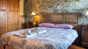Ein Schlafzimmer mit Steinwand, Holzbettgestell und einem Bett mit aufgerollten Handtüchern.