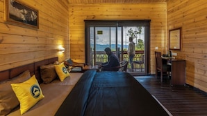 A wooden cabin with a bed, a desk, and a view of mountains. - The Hosteller Kasar Devi (Almora)