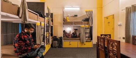A dormitory room with bunk beds, a dining table, and chairs.