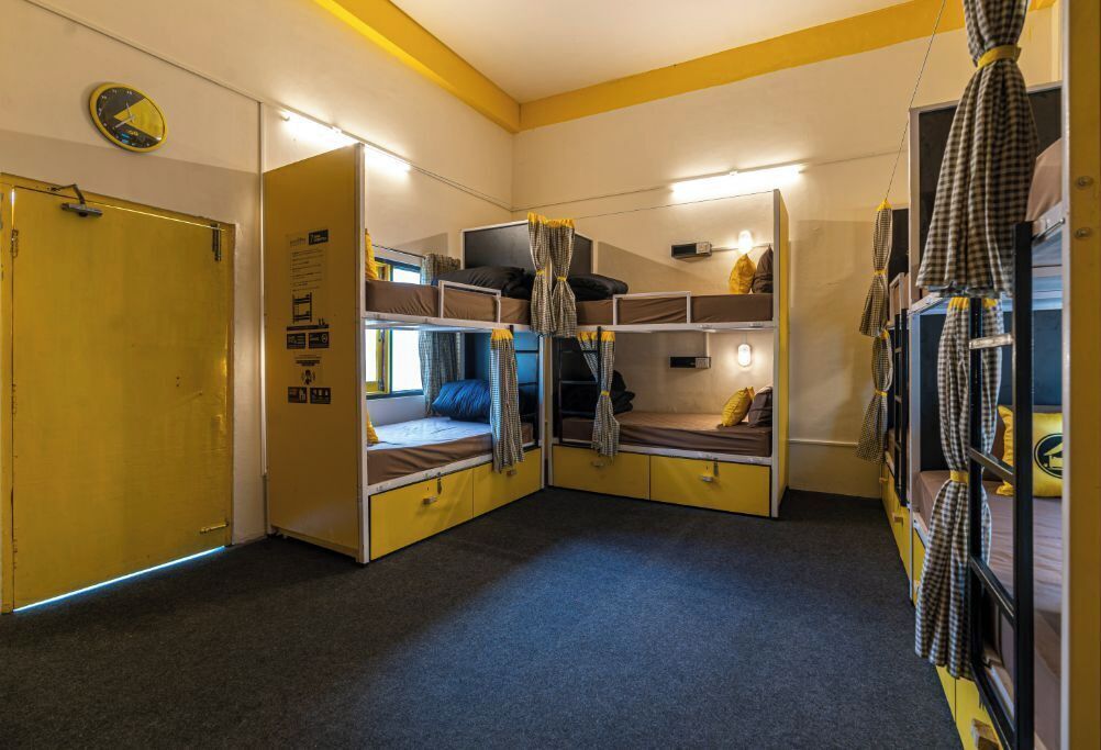 A dormitory room with bunk beds, a clock on the wall, and a door.