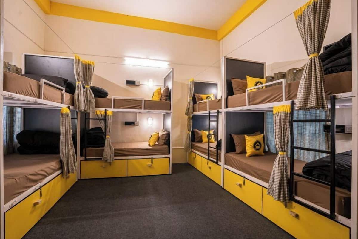 A dormitory room with bunk beds, each with a mattress, pillows, and a blanket.