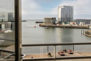 A view of a waterfront with a building under construction, a dock with boats, and a clear sky. - Luxury apartment, Scheveningen (Scheveningen)