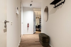 A hallway with a wooden floor, a fire extinguisher, a bench, and a wall-mounted shelf.