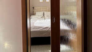 A wooden door with frosted glass panels leading to a bedroom with a bed, a headboard, and two framed pictures on the wall.