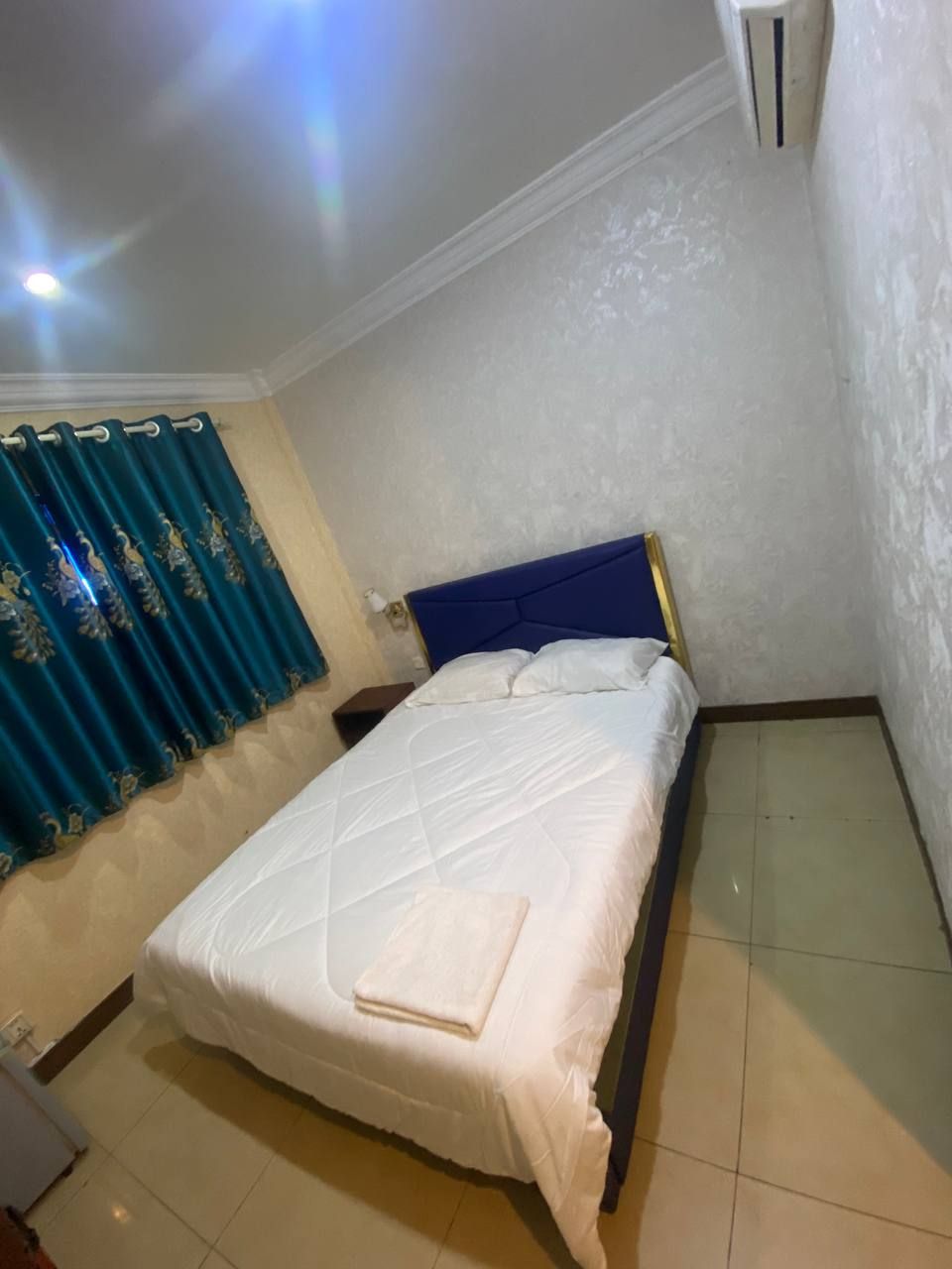 A single bed with a blue headboard in a room with white walls and a tiled floor.