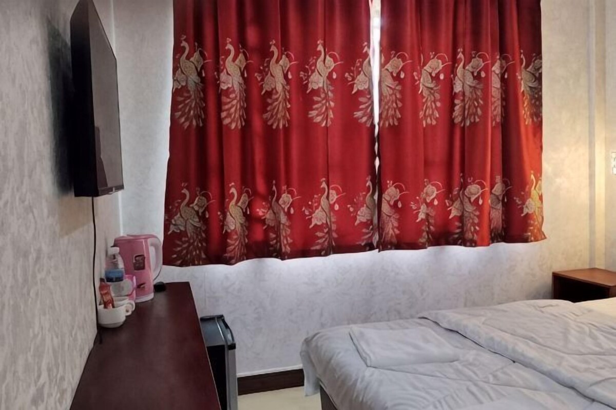 A hotel room with a bed, a desk with a coffee maker, and a TV mounted on the wall.