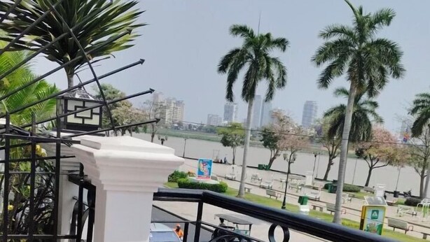 A balcony with a checkered floor, a metal railing, and a view of a cityscape with palm trees. - TWILIGHT INN (Phnom Penh)