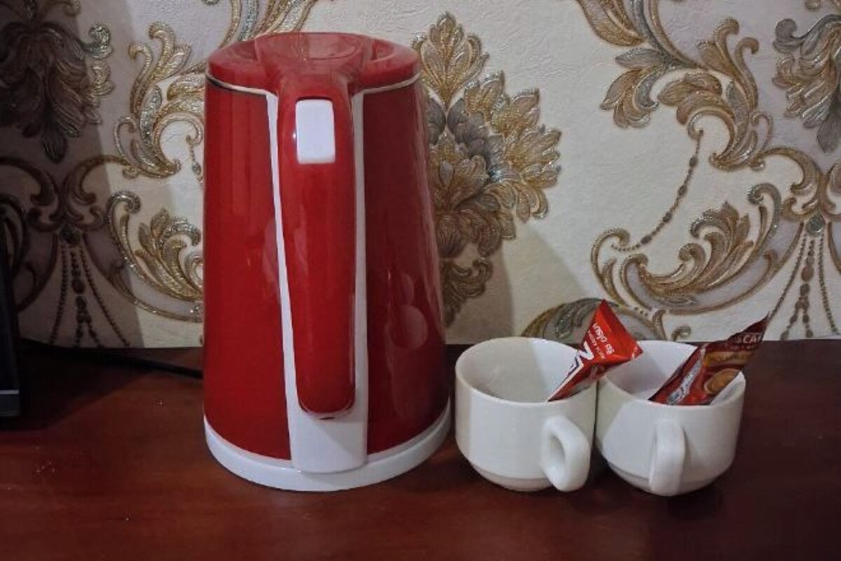 A red kettle, a white mug, and a mug with a packet of tea on a wooden table.