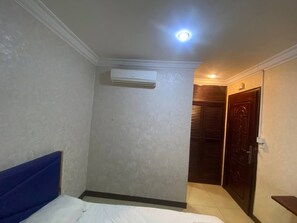 A hotel room with a bed, an air conditioning unit, a door, and a ceiling light. - TWILIGHT INN (Phnom Penh)