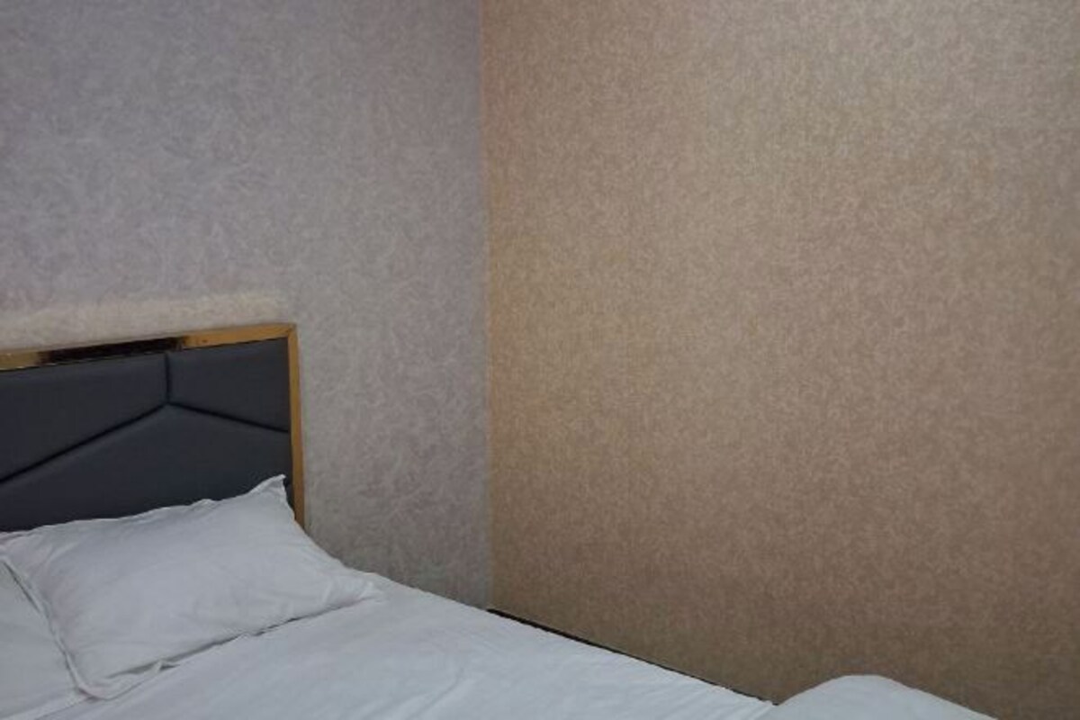 A bed with a headboard, a wall with a textured pattern, and a plain wall.