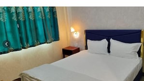 A hotel room with a bed, a nightstand, a lamp, and a window with curtains. - TWILIGHT INN (Phnom Penh)