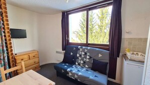 A small room with a sofa, a wooden dresser, a television, and a window with curtains.