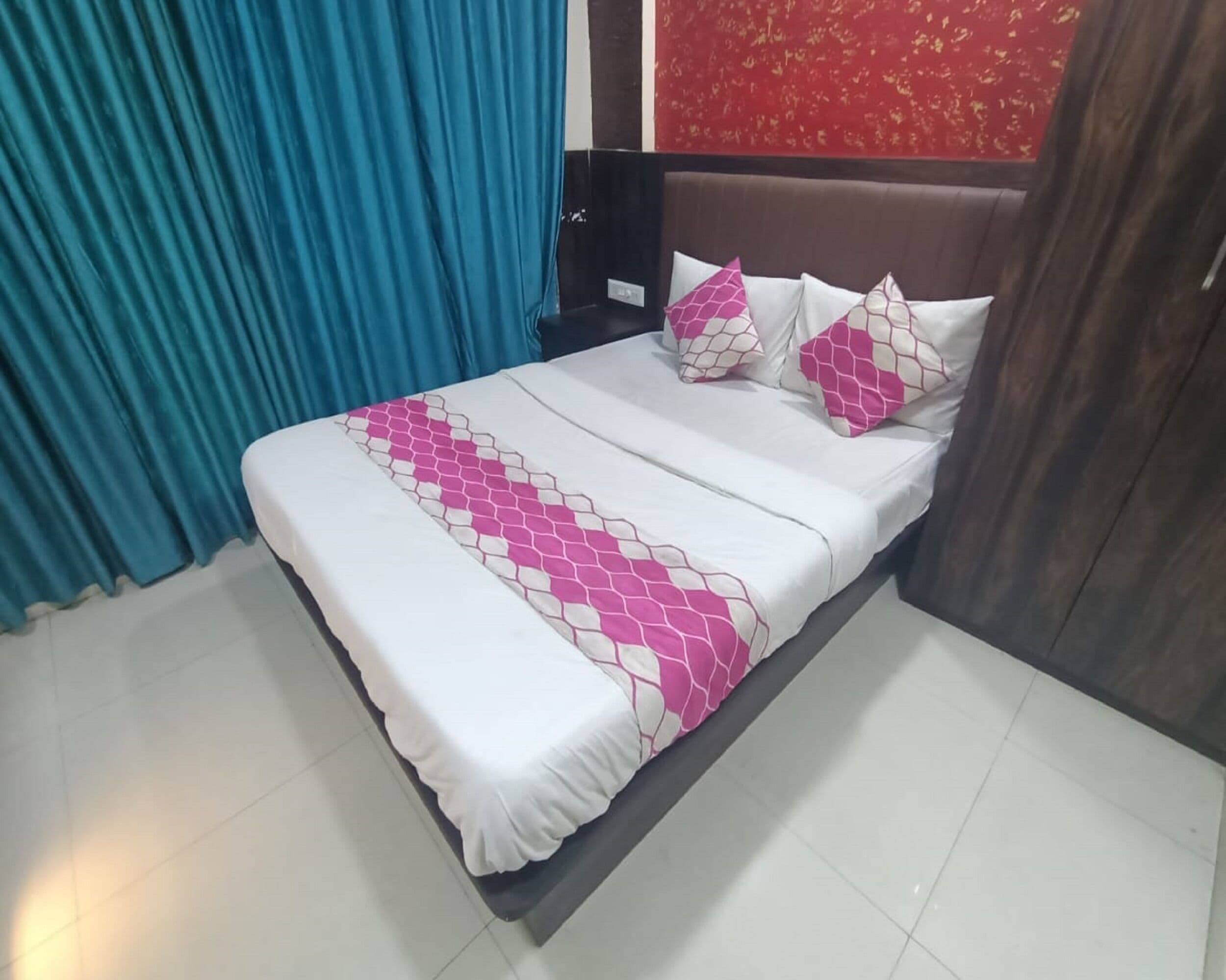 A neatly made bed with a white and pink patterned bedspread, a brown headboard, and a blue curtain to the left.