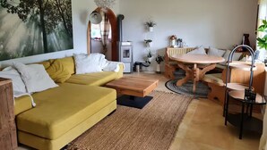 Un salon avec un canapé jaune, une table ronde en bois et un grand tableau représentant une forêt.