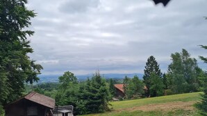 Un chalet rustique doté d’une terrasse en bois, entouré d’une végétation luxuriante et offrant une vue lointaine sur les montagnes.