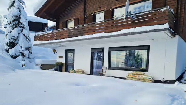 Une cabane en bois dotée de grandes fenêtres et entourée d’un paysage enneigé.