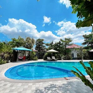 A swimming pool with lounge chairs and umbrellas, surrounded by trees and a building with a red roof. - Kampot Orkide Boutique (Kampot)