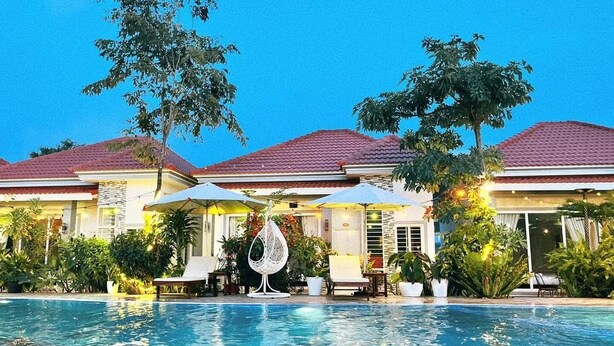 A swimming pool with lounge chairs and umbrellas, surrounded by a building with a red-tiled roof and lush greenery. - Kampot Orkide Boutique (Kampot)