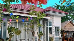 A house with a red-tiled roof, a thatched-roof structure, and colorful triangular flags. - Kampot Orkide Boutique (Kampot)