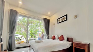 A hotel room with a large bed, a bedside table, a window with curtains, and a view of the outside. - Kampot Orkide Boutique (Kampot)