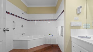 A bathroom with a bathtub, shower, and toilet. There are steps leading to the bathtub, and a towel rack is visible. - Romantic King Spa Suite Perfect for Couples in Coffs Harbour (Coffs Harbour)