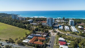 An aerial view of a coastal area with multiple buildings, including high-rise hotels and residential structures, surrounded by greenery and a beach. - Romantic King Spa Suite Perfect for Couples in Coffs Harbour (Coffs Harbour)