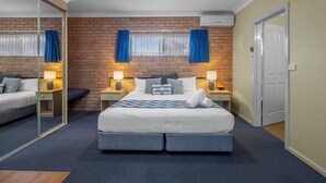 A modern bedroom with a brick wall, a large bed with a blue and white checkered bedspread, two bedside lamps, and a mirror on one wall. - Romantic King Spa Suite Perfect for Couples in Coffs Harbour (Coffs Harbour)