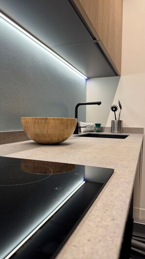 Une cuisine moderne avec un saladier en bois posé sur le plan de travail, un robinet noir et une plaque de cuisson à induction au design épuré.