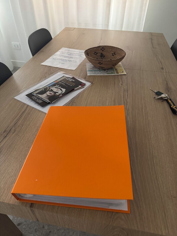 Une table en bois sur laquelle se trouvent un grand dossier orange, un panier en osier, des clés et quelques papiers.