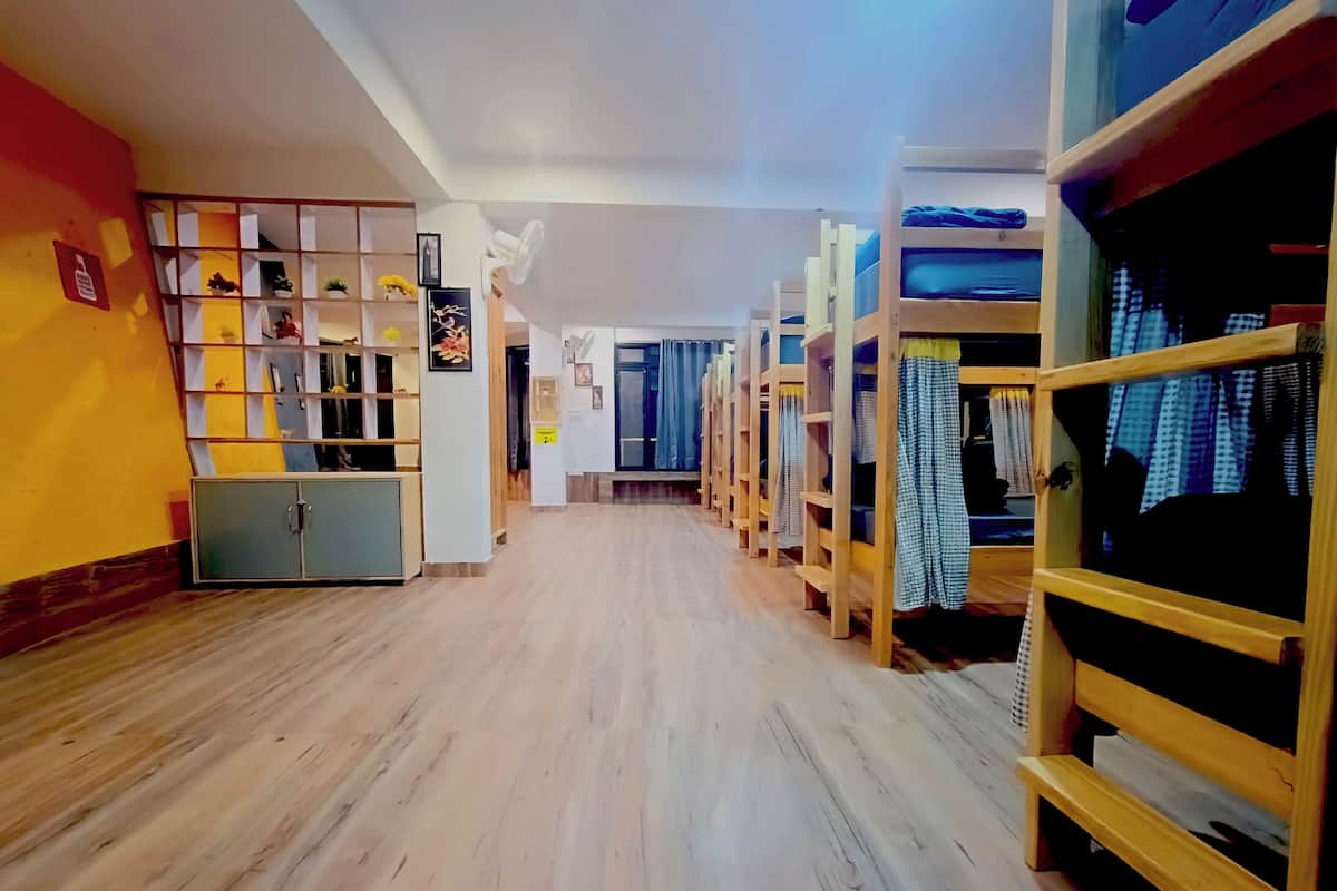 A hotel corridor with wooden bunk beds on the right, a storage unit on the left, and a wooden floor.