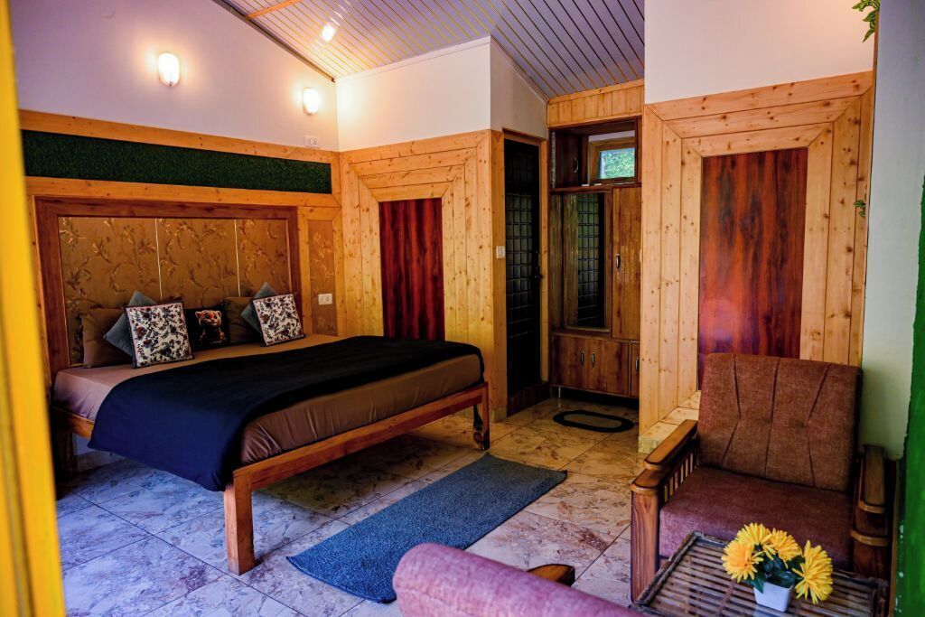 Una habitación de madera con una cama, una silla y una pequeña mesa con flores.