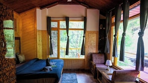 A cozy cabin room with a bed, a chair, a small table, and a window with curtains. - The Hosteller Mussoorie By The Streamside, Kempty (Mussoorie)
