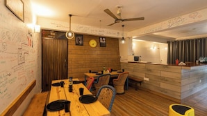 A dining area with wooden tables and chairs, a kitchen area with a counter, and walls covered with writings and drawings. - The Hosteller Mussoorie By The Streamside, Kempty (Mussoorie)
