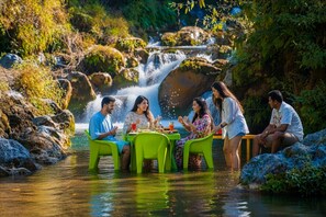 A group of people sitting at a table by a waterfall in a natural setting. - The Hosteller Mussoorie By The Streamside, Kempty (Mussoorie)