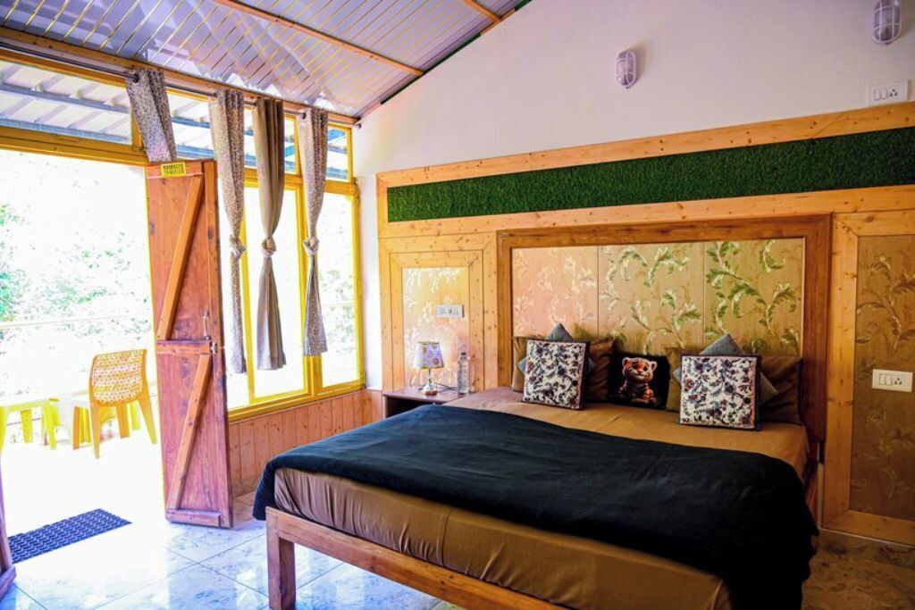 Un dormitorio con cama, cortinas, cabecera de madera, una mesita y una silla.