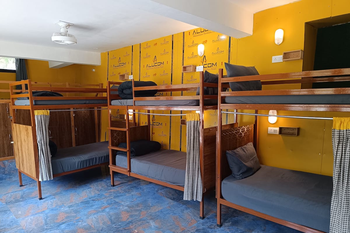 A dormitory room with bunk beds, wooden furniture, and a blue-tiled floor.