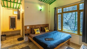 A bedroom with a wooden bed, a nightstand, a window with a view of trees, and a green ceiling. - The Hosteller Mussoorie By The Streamside, Kempty (Mussoorie)