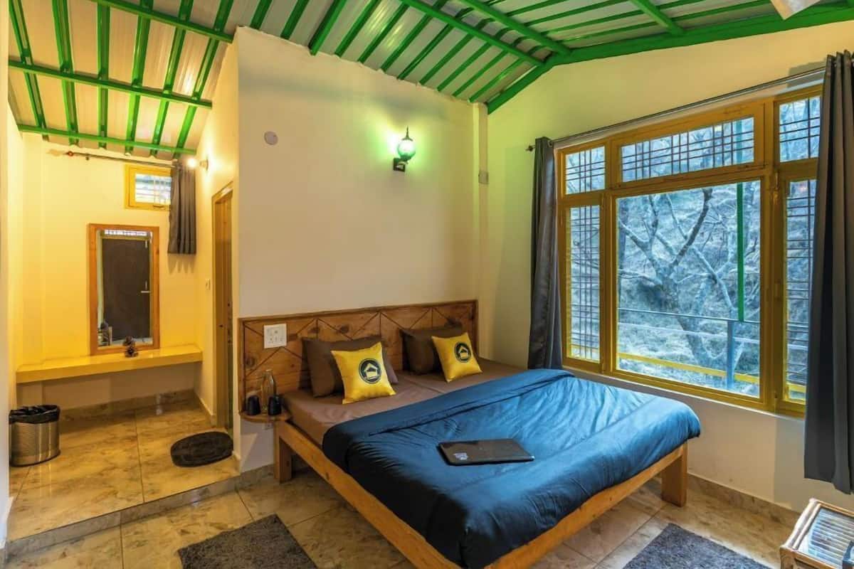 A bedroom with a wooden bed, a nightstand, a window with a view of trees, and a green ceiling.