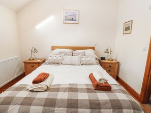 Un letto rifatto con una coperta a quadri, due comodini con lampade e un quadro incorniciato appeso al muro.