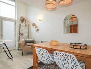 A modern dining area with a wooden table, white chairs, a mirror, and wicker pendant lights. - Trenethick (Truro)