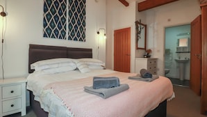 Ein Schlafzimmer mit Bett, Nachttischen, einem Kleiderschrank, einem Spiegel und einem durchgehenden Türspalt sichtbaren Badezimmer.