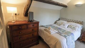 A bedroom with a wooden dresser, a bed with patterned bedding, and exposed wooden beams on the ceiling.