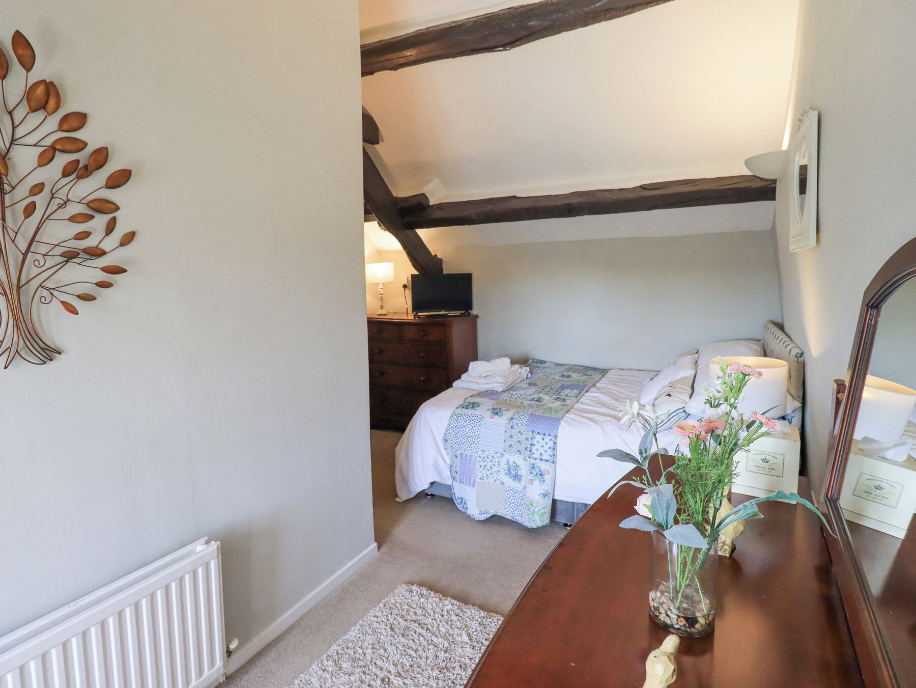 A bedroom with a bed, a dresser, a mirror, and a decorative metal wall piece.