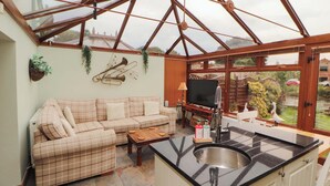 A conservatory with a sofa, television, and kitchen area. - Beckside Cottage (Penrith)